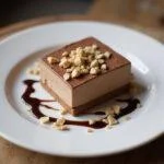 Serving a velvety hazelnut cream swirl dessert garnished with crushed hazelnuts and chocolate sauce on a rustic table.