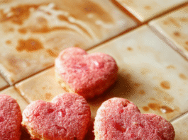 Heart Shaped Romantic Valentine Cookies Handmade pink heart-shaped sugar cookies with white chocolate drizzle and red velvet dusting, on a white marble board surrounded by fresh roses and edible glitter, bright natural light, shallow depth of field, soft shadows.