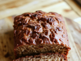 Moist Foolproof Banana Bread Recipe A golden-brown loaf of banana bread resting on a rustic wooden cutting board, sliced to reveal a tender, moist crumb with visible banana fragments and a subtle caramelized crust, dusted lightly with powdered sugar.