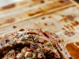 A golden-brown, fall-apart tender pot roast served in its rich, savory au jus, surrounded by soft pearl onions, baby carrots, and creamy garlic butter potatoes, garnished with fresh parsley on a rustic wooden board.